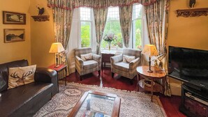 A traditional living room with a fireplace, two armchairs, a sofa, and a television. - 4 bedroom accommodation in Aberfeldy (Aberfeldy)