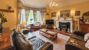 A traditional living room with leather sofas, a fireplace, and a chandelier. - 4 bedroom accommodation in Aberfeldy (Aberfeldy)
