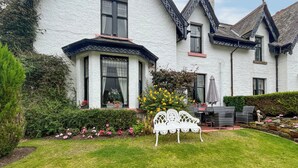 A white house with a bay window, a garden with a white bench, and a statue. - 4 bedroom accommodation in Aberfeldy (Aberfeldy)