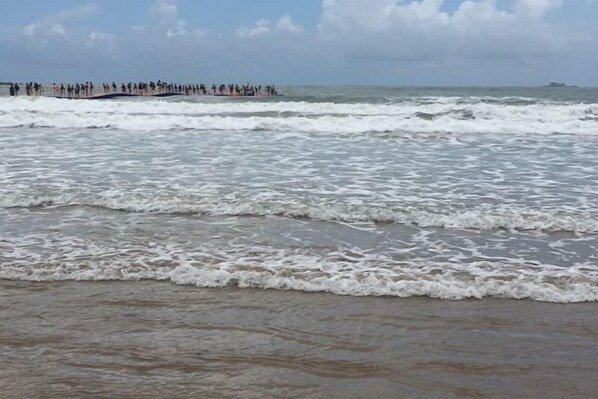 Una playa con olas y un muelle al fondo.