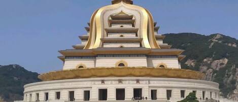 A large, multi-tiered building with a circular base, surrounded by a spacious open area.