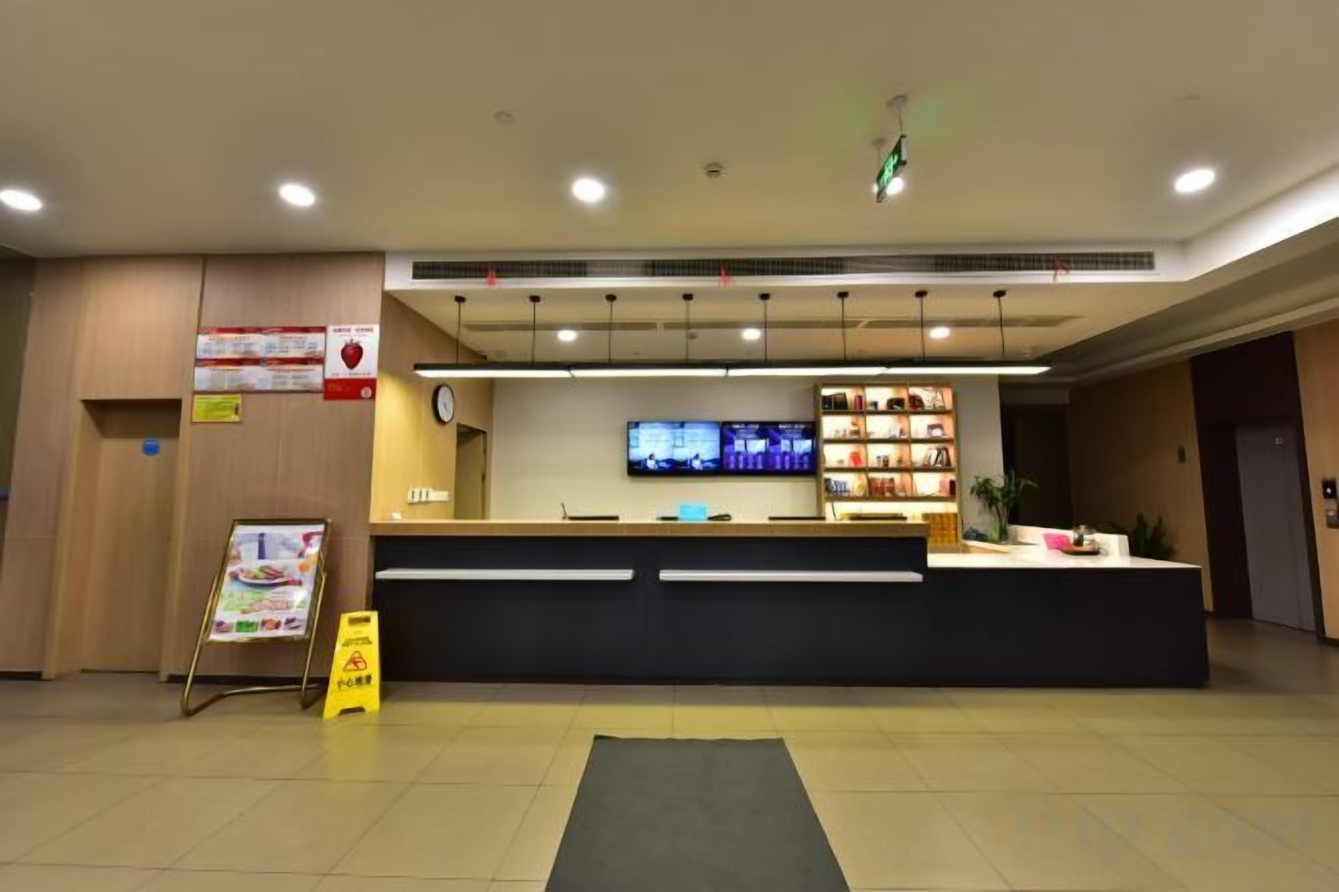 A hotel reception area with a reception desk, a television screen, and a shelf with various items.