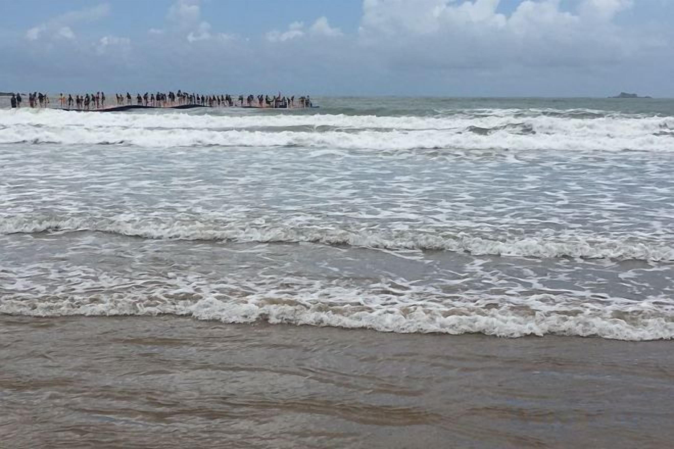 Una playa con olas y un muelle a lo lejos.