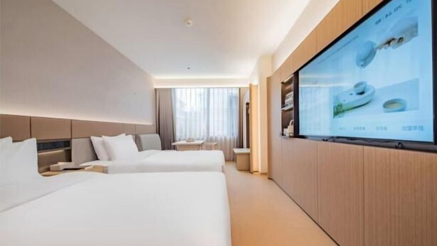 Een hotelkamer met twee bedden, een televisie aan de muur en een raam met gordijnen.