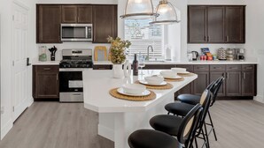 Een moderne keuken met donkere houten kasten, een wit kookeiland met zitplaatsen, roestvrijstalen apparatuur en hanglampen.