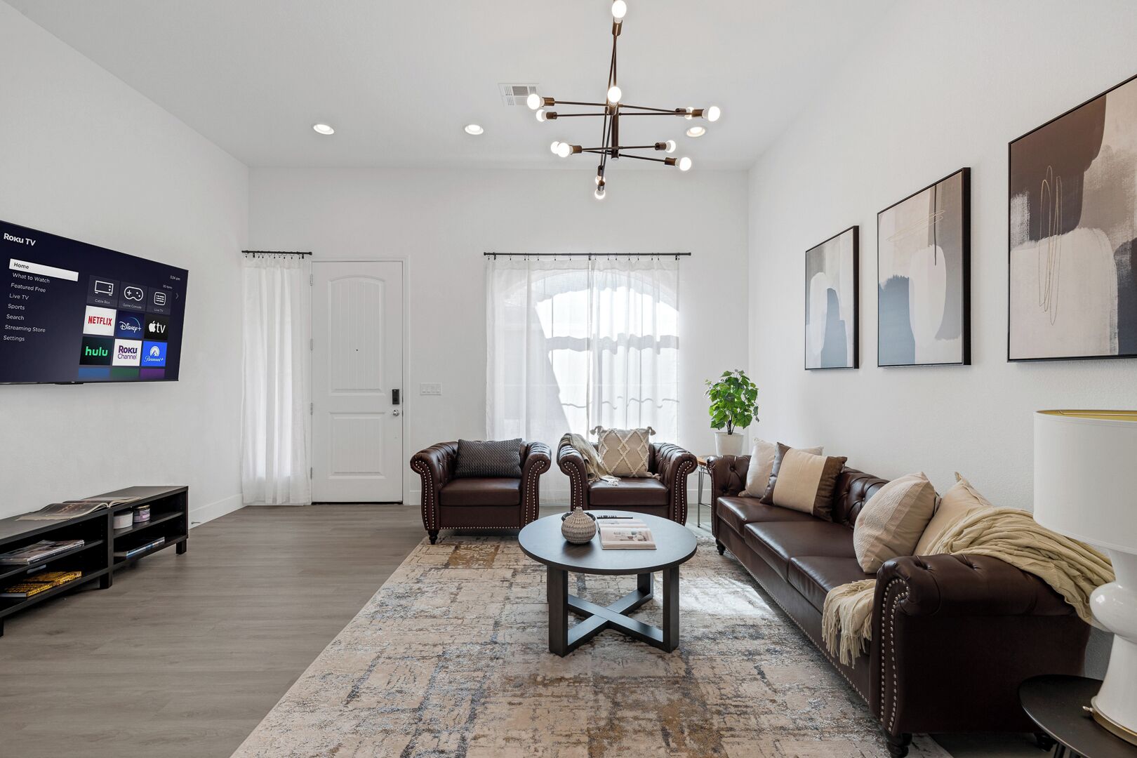A modern living room with a flat-screen TV, leather sofas, a coffee table, and artwork on the walls.
