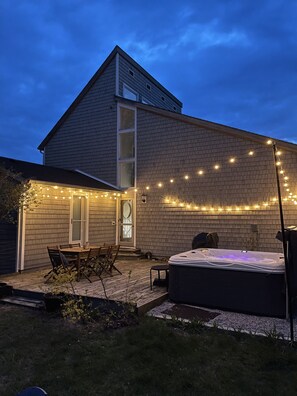 A two-story house with a brick exterior, a wooden deck, a hot tub, and string lights. - Steps to Village & Lake * Hot Tub * Pets Welcome (Northport)
