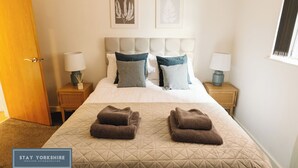 A hotel room with a bed, two bedside tables with lamps, a door, and two framed leaf artworks on the wall.