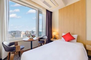 A hotel room with a large window, a bed with white and red pillows, a small table with chairs, and a lamp. - Shin Shin Hotel Jeju Worldcup (Seogwipo)