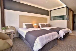 Une chambre d’hôtel avec deux lits, une petite table avec une chaise et un grand miroir.