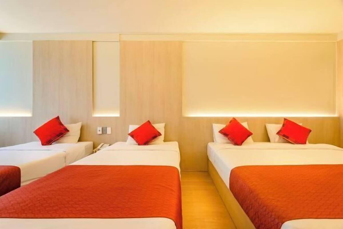 Une chambre d’hôtel avec deux lits simples, chacun agrémenté d’un oreiller rouge et d’une couverture blanche.