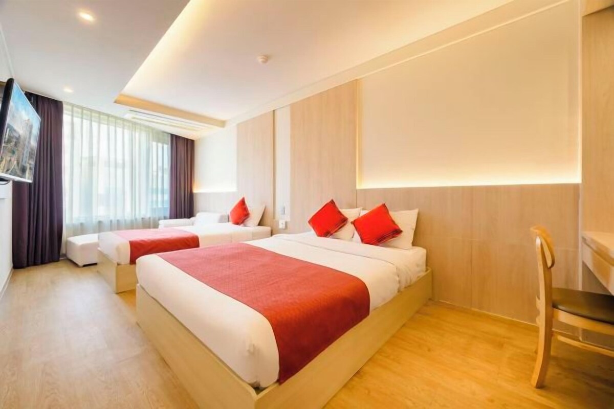 A hotel room with two beds, a TV, and a wooden floor.