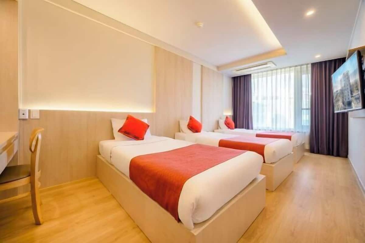 Une chambre d’hôtel avec deux lits, chacun agrémenté d’un oreiller rouge, d’une chaise en bois et d’une grande fenêtre avec des rideaux.