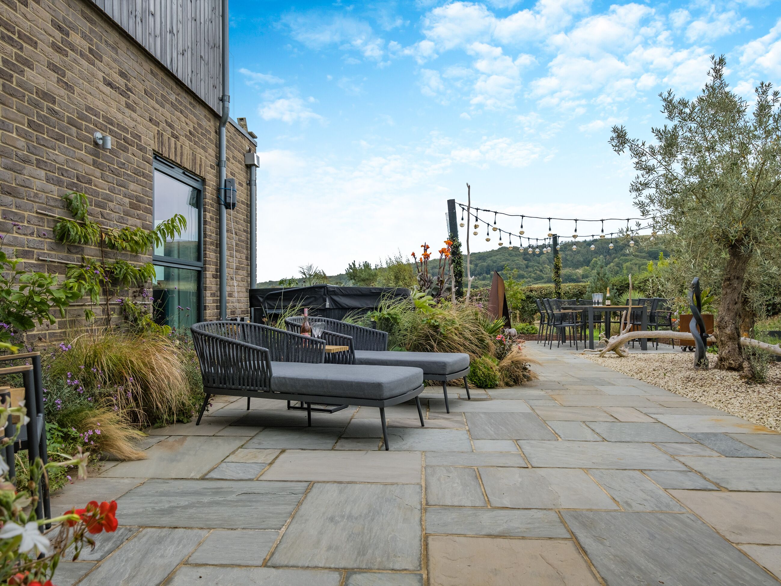 A patio with outdoor seating, a brick building, and a view of the hills.