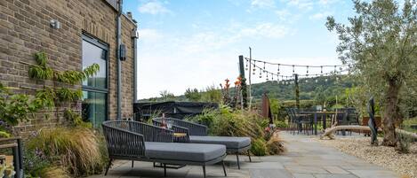 A patio with outdoor seating, a brick building, and a view of the hills.