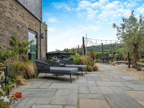 A patio with outdoor seating, a brick building, and a view of the hills.