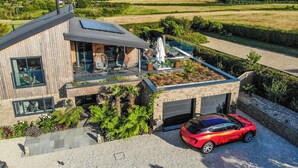A modern house with a flat roof, a covered outdoor seating area, and a red sports car parked in the driveway. - 5 bedroom accommodation in Totland (Totland)