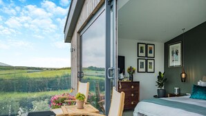 A bedroom with a bed, a dresser, a chair, a table, and a view of a green landscape through a glass door. - 5 bedroom accommodation in Totland (Totland)