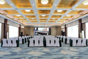A conference room with rows of chairs, a long table, and a large screen at the front.
