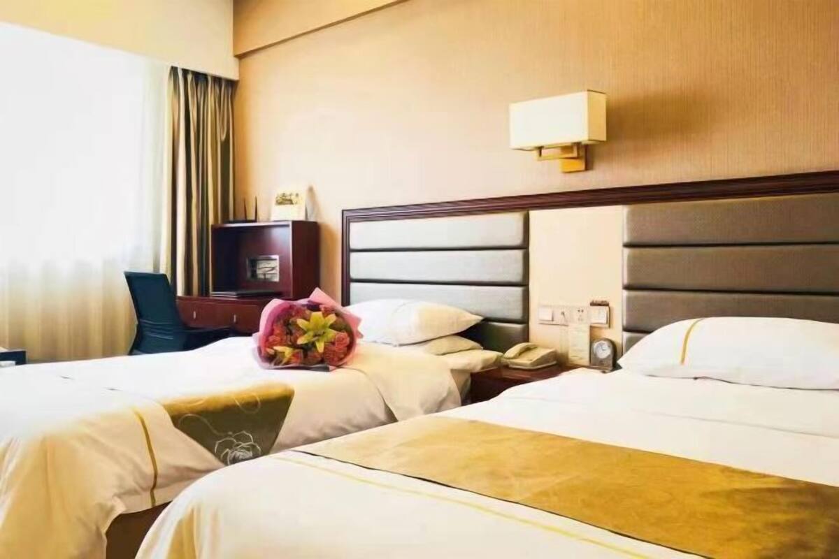 Une chambre d’hôtel avec deux lits, un bureau, une chaise, une lampe et une fenêtre avec des rideaux.