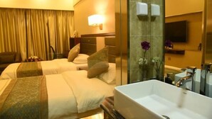 Habitación de hotel con dos camas, un baño grande con lavamanos y un televisor montado en la pared.