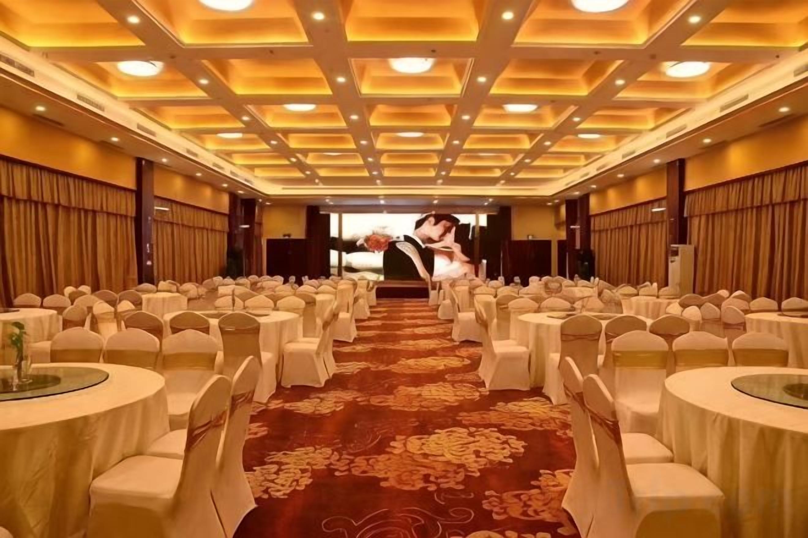 Un salón de banquetes con filas de mesas redondas, cada una con mantel blanco y sillas a juego, dispuestas para un evento formal.