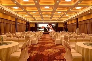Un salón de banquetes con filas de mesas redondas, cada una con mantel blanco y sillas a juego, dispuestas para un evento formal.
