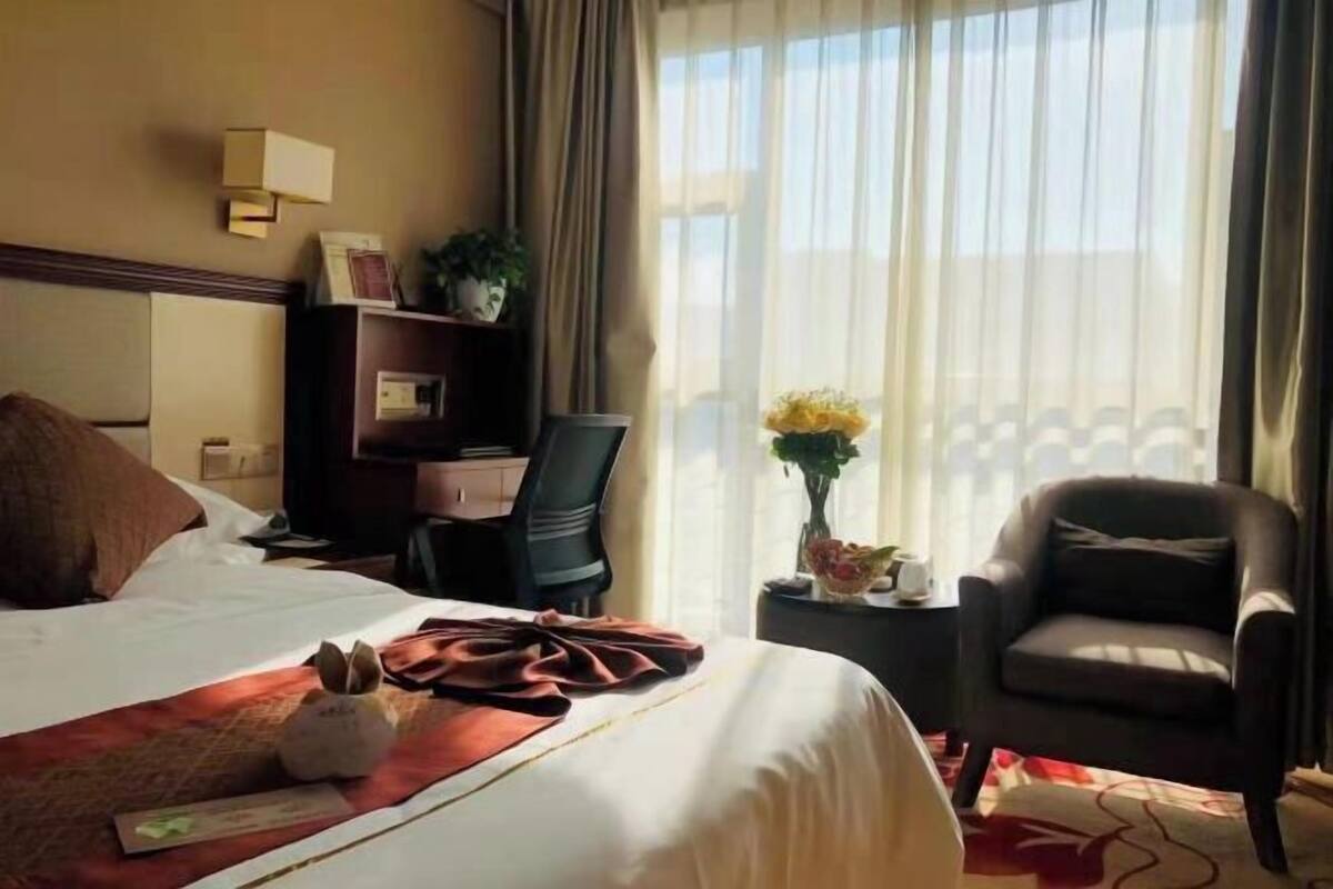 Une chambre d’hôtel avec un lit, un bureau, une chaise et une fenêtre avec des rideaux.