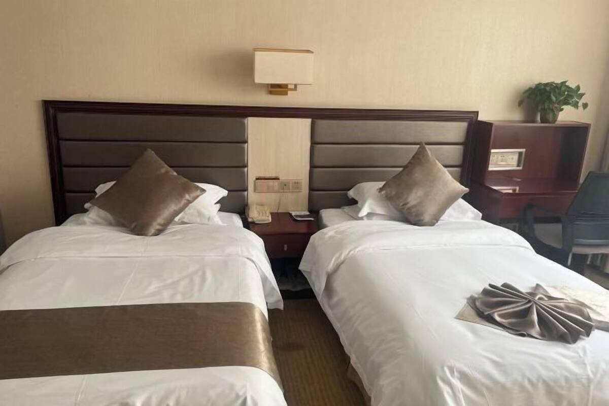 Une chambre d’hôtel avec deux lits, une table de chevet, une lampe et un bureau agrémenté d’une plante.