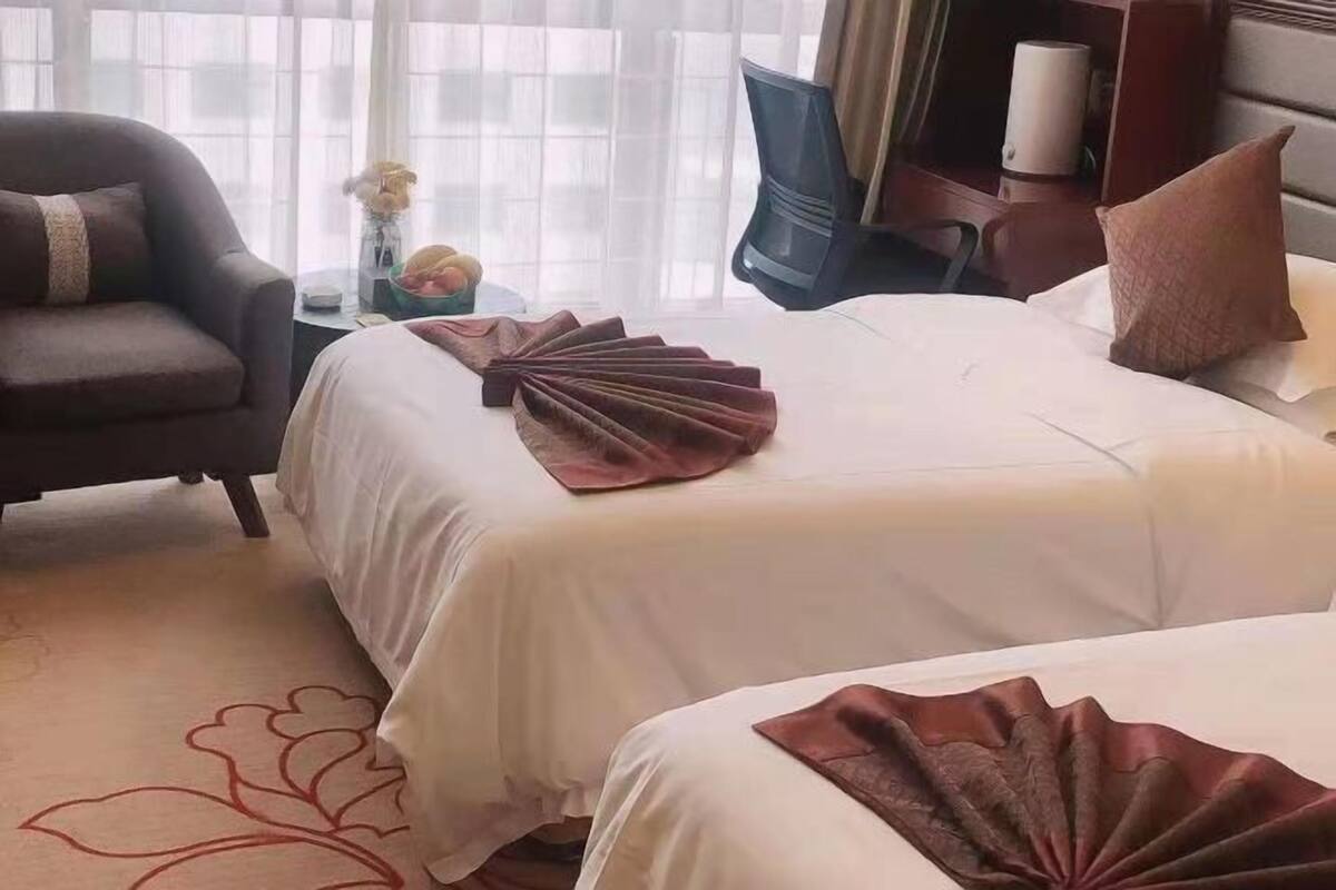 Une chambre d’hôtel avec deux lits, un canapé, une télévision et un bureau agrémenté d’un vase et de fleurs.
