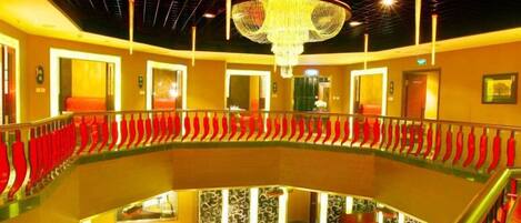 A multi-level hotel lobby with a central staircase, a chandelier, and red seating areas.