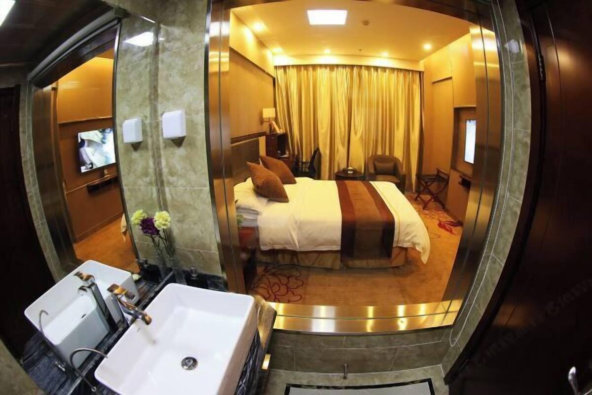 Une chambre d’hôtel comprenant un lit, un bureau, une chaise, une télévision et une salle de bain avec un lavabo et un miroir.