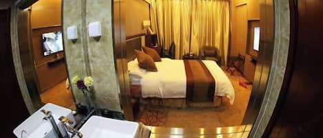 A hotel room with a bed, a desk, a chair, a TV, and a bathroom with a sink and mirror.