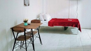 A room with a bed covered in a red blanket, a small table with a chair, and a wall-mounted TV. - Reddoorz @ Rio Bella Lacson St. Bacolod (Bacolod)