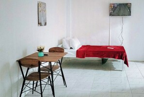 A room with a bed covered in a red blanket, a small table with a chair, and a wall-mounted TV. - Reddoorz @ Rio Bella Lacson St. Bacolod (Bacolod)