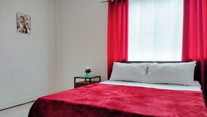 Une chambre à coucher avec un lit, des rideaux rouges, une petite table avec une plante et un tableau accroché au mur.