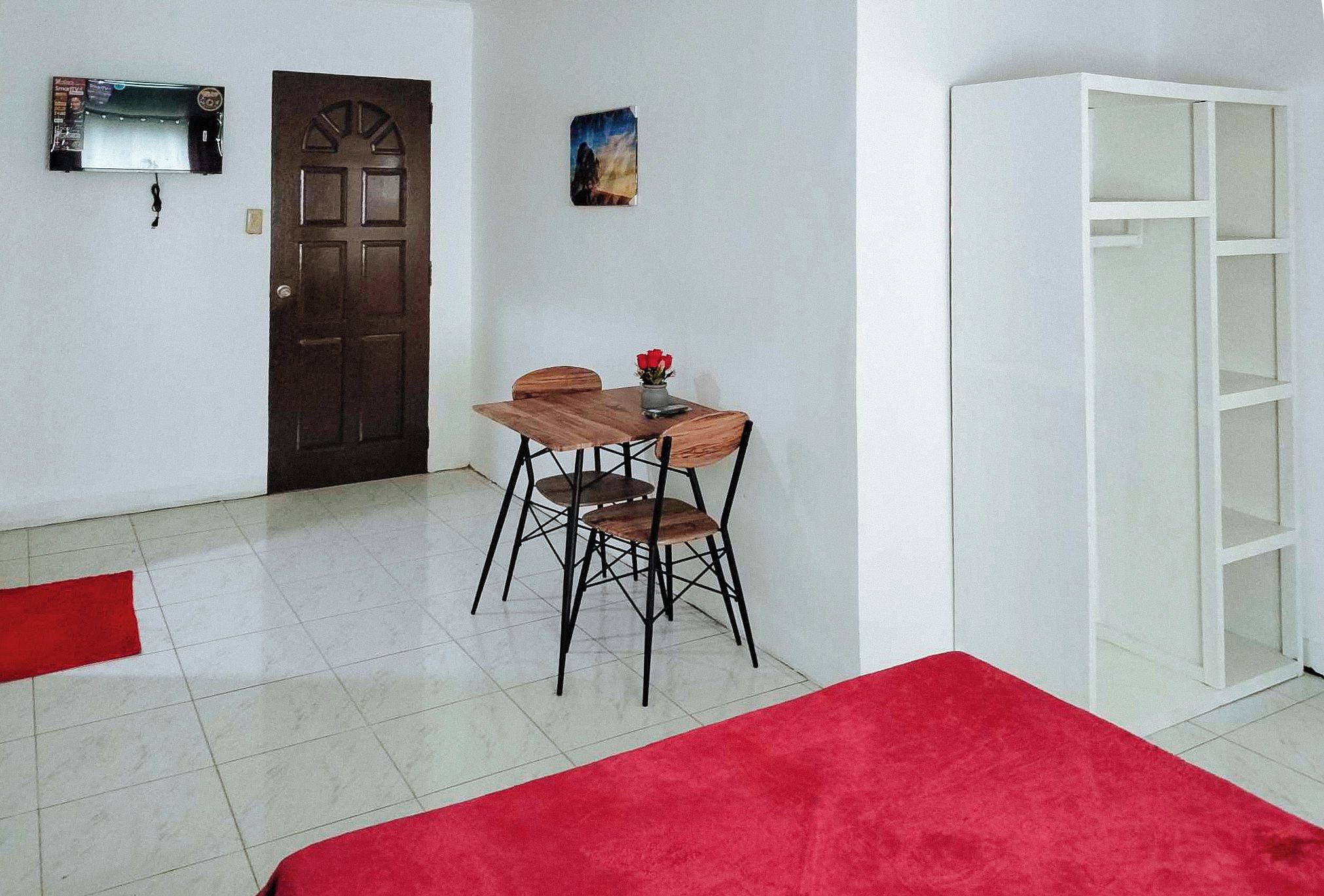 Une pièce comprenant une table et des chaises de salle à manger en bois, une moquette rouge, un meuble blanc et une porte ornée d’un panneau décoratif.