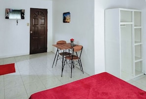 A room with a wooden dining table and chairs, a red carpet, a white cabinet, and a door with a decorative panel.