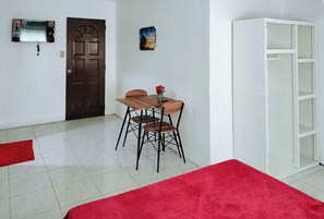 Una habitación con una mesa y sillas de madera, una alfombra roja, un armario blanco y una puerta con un panel decorativo.