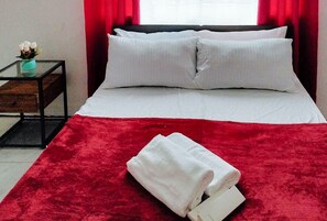 Un lit bien fait, avec des draps et des oreillers blancs, un plaid rouge et une serviette blanche pliée posée sur le lit.
