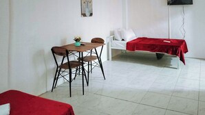 A room with a dining table, two chairs, a bed with a red blanket, a white sofa, and a wall-mounted TV. - Reddoorz @ Rio Bella Lacson St. Bacolod (Bacolod)