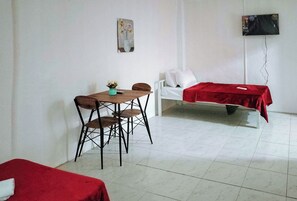 A room with a dining table, two chairs, a bed with a red blanket, a white sofa, and a wall-mounted TV. - Reddoorz @ Rio Bella Lacson St. Bacolod (Bacolod)