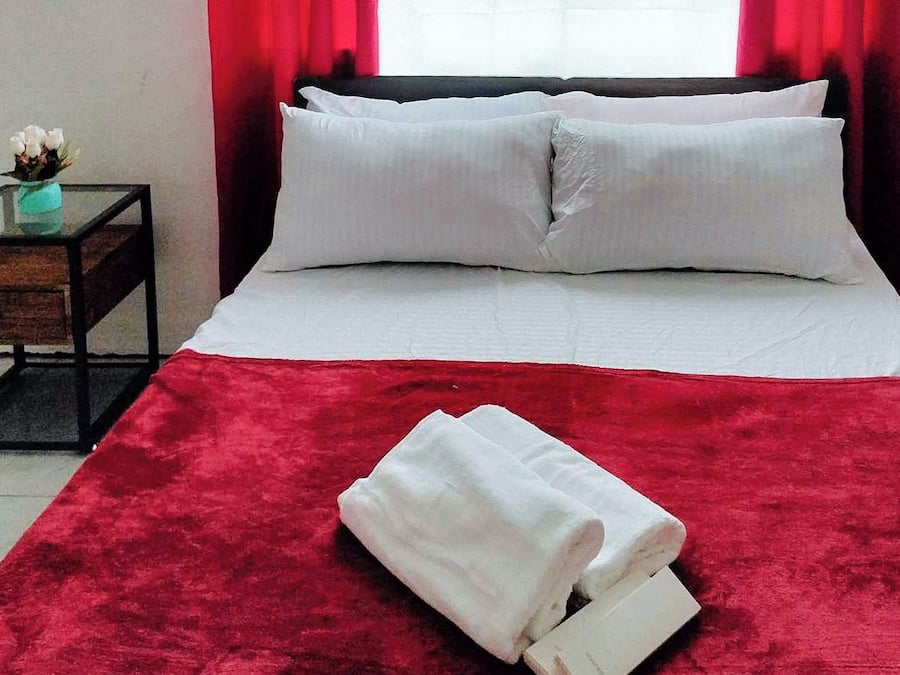 A neatly made bed with white linens and pillows, a red throw blanket, and a folded white towel on the bed.