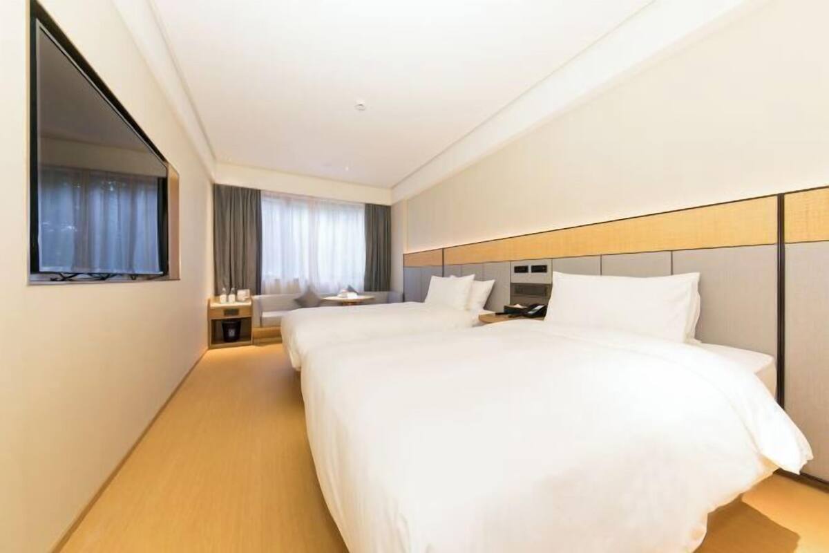 A hotel room with a large bed, bedside tables, a mirror, and a window with curtains.