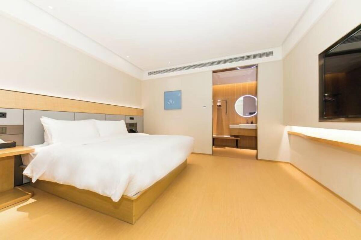 A modern hotel room with a large bed, bedside tables, a built-in desk, and a bathroom with a mirror.