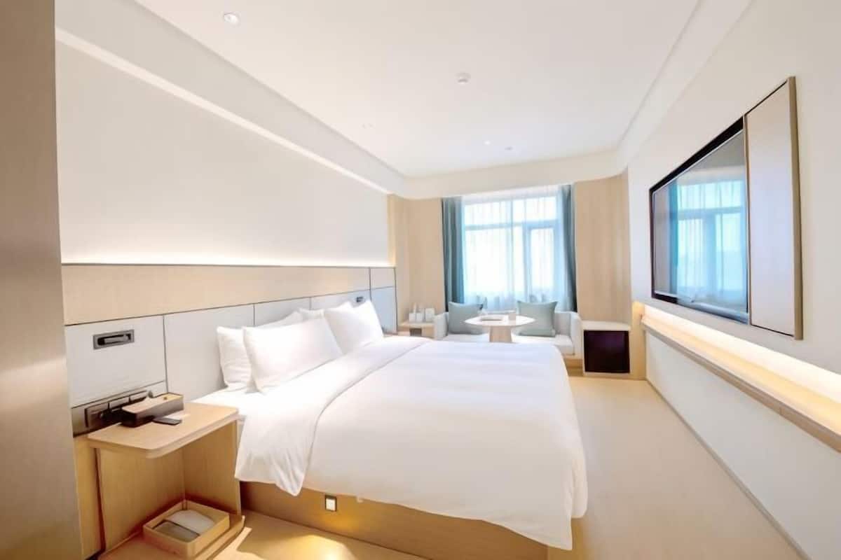 A modern hotel room with a large bed, bedside tables, a TV, and a window with curtains.