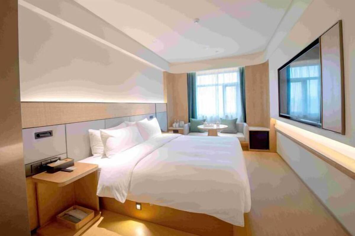 A modern hotel room with a large bed, bedside tables, a TV, and a window with curtains.