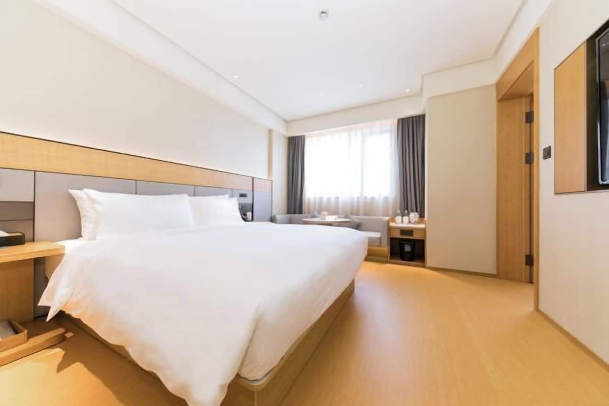 A hotel room with a large bed, bedside tables, a desk, and a window with curtains.