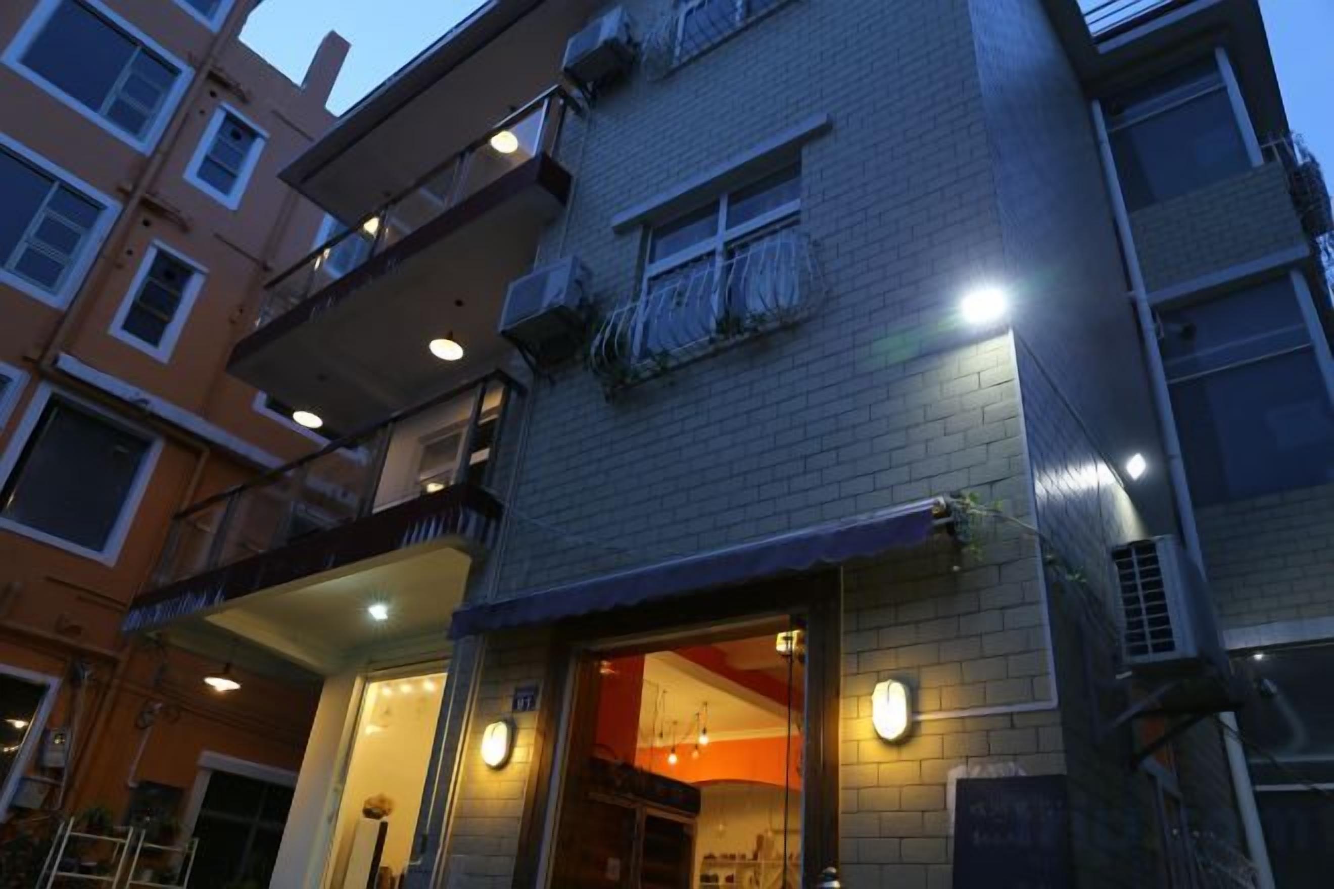 A multi-story building with a ground-floor entrance, balconies, and a visible interior space with a warm light.