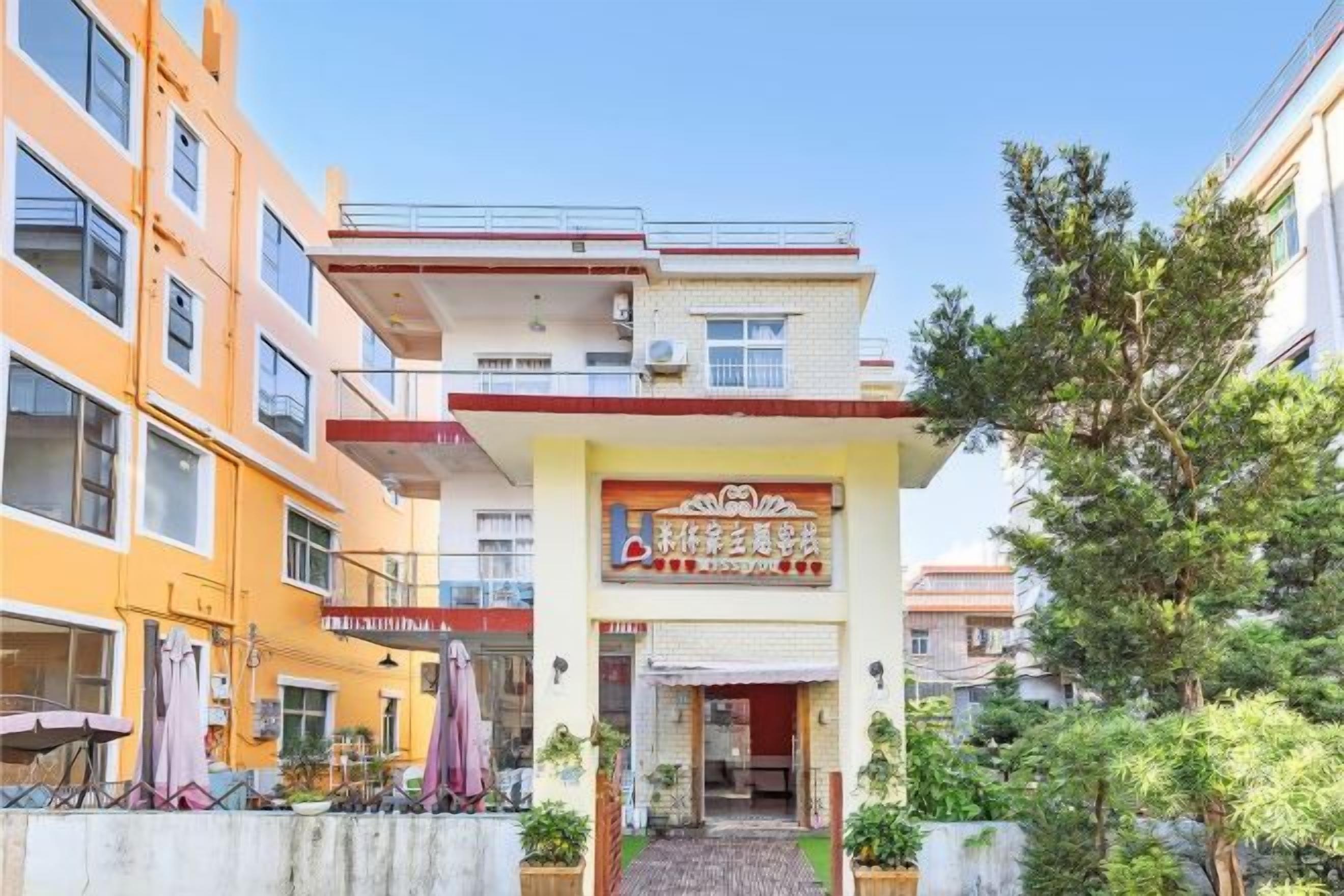 Un edificio de varios pisos con entrada a nivel de calle, un letrero de restaurante visible y un pequeño área de asientos al aire libre con sombrillas.